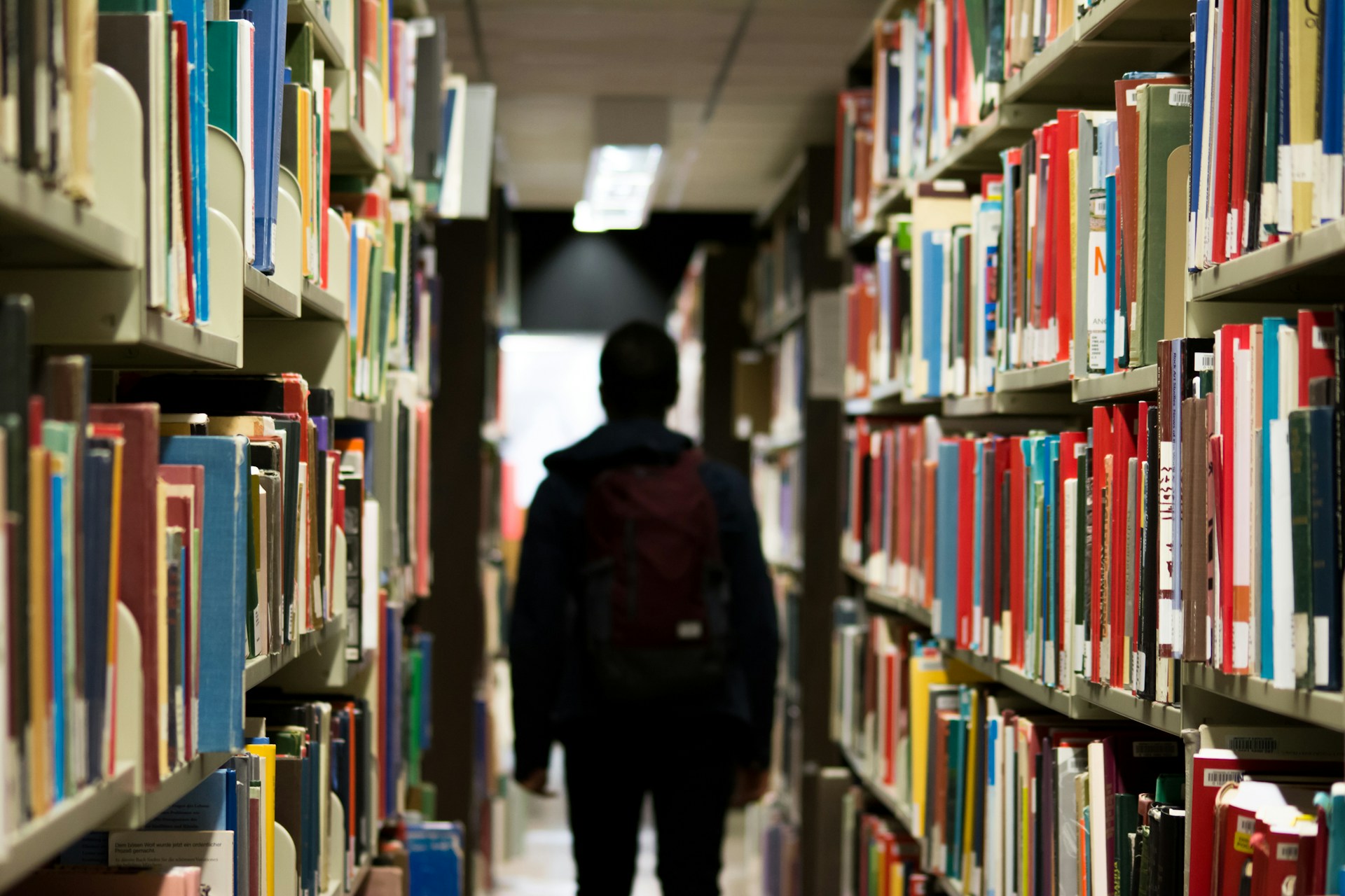 Image of a person walking between shelves of books in a library.