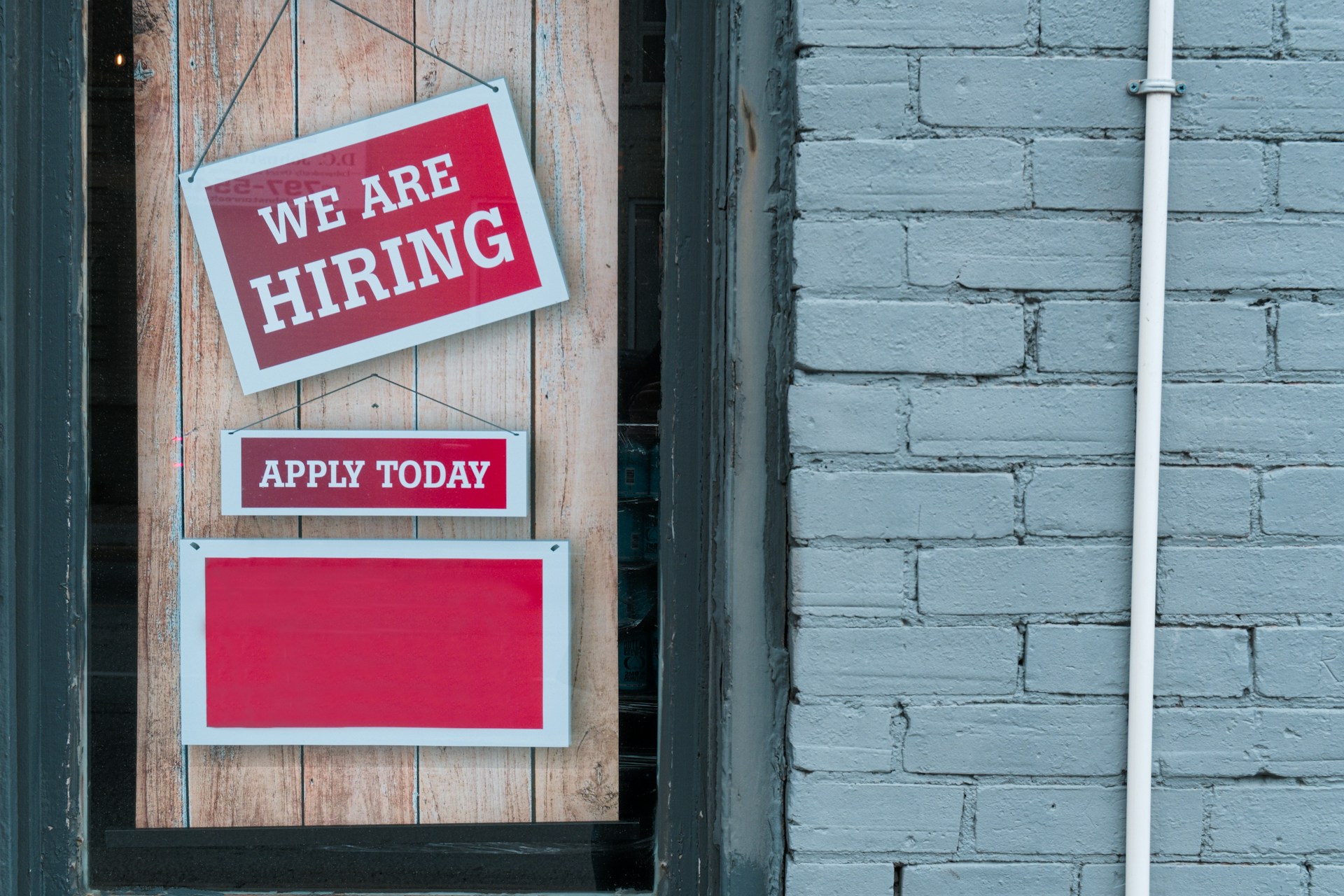 Image of a red sign in a window that says "We are hiring. Apply today."